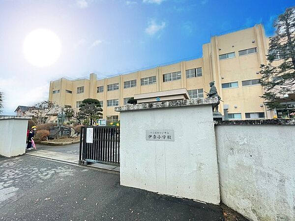 伊奈小学校 青空の下、穏やかな光を浴びて、歴史を刻む校舎が静かに佇んでいます。子どもたちの元気な声が響き渡るであろう、温かく安心感のある学び舎の入り口が、未来への希望を感じさせます （1100m）