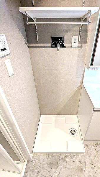 【洗濯機置き場】清潔感ある洗面室の洗濯機置場スペース。上部には可動式のハンガーバー付き棚を設置しており、洗剤類の収納やちょっとした部屋干しにも便利に活用できます。