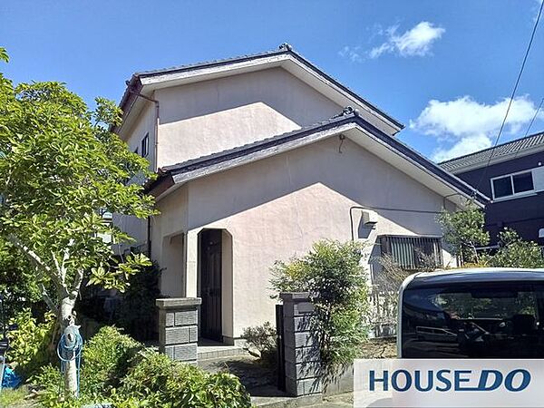 切妻屋根と玄関まわりを写した外観。庭木のある落ち着いた佇まい。