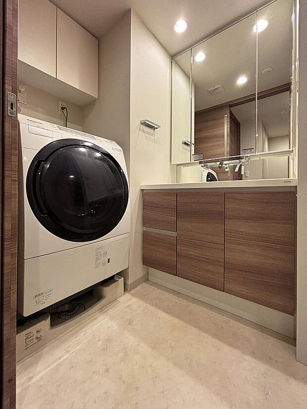 三面鏡収納付き化粧洗面台、洗剤等を収納できる吊り戸棚が配置された洗面スペース。