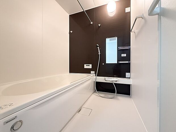 【浴室】ダークブラウンのアクセントウォールが洗練された印象を与える浴室。ゆったりとした浴槽で、家族の絆を深めるひとときを。