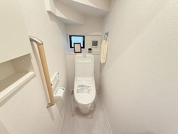 1階トイレ。手洗い付きのトイレなので手を洗うこともでき、また、タオルを設置できるタオル掛け付き。トイレ内は小窓付きで換気がしやすく、予備のトイレットペーパーを置けるスペースもあります。