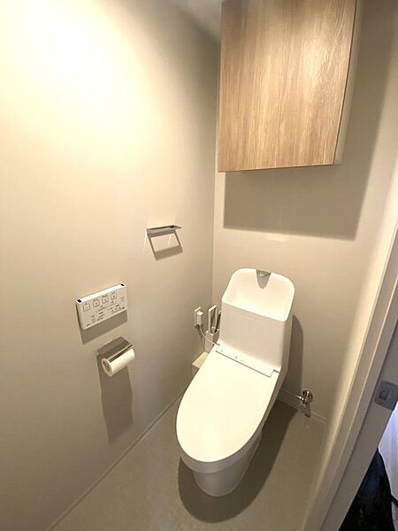 清潔感あふれる温水洗浄機能付きのトイレ空間です。壁面には操作が簡単なリモコンパネルを設置し、上部にはトイレットペーパーや掃除用品などをスッキリ収納できる便利な吊戸棚を備えています。