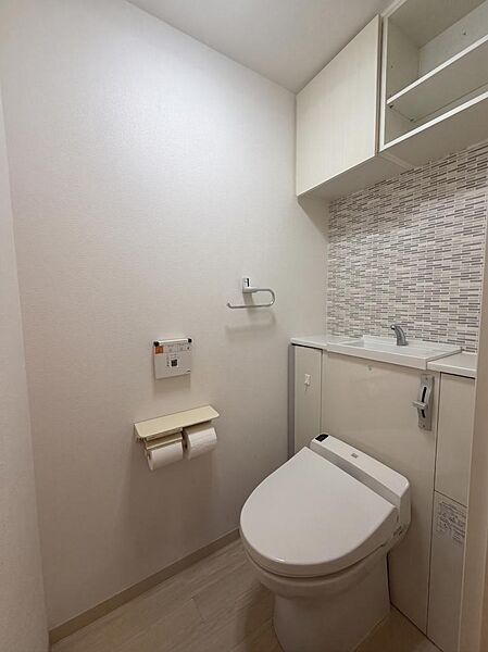 温水洗浄便座を標準装備した清潔感のあるトイレ空間です。手洗いに便利な専用カウンターと、トイレットペーパーや清掃用品をすっきりと収納できる吊戸棚収納が備わっており使い勝手良好です。