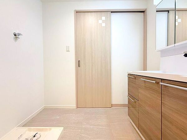 【洗面所】ナチュラルな木目調のデザインが温かみを感じさせる洗面脱衣所です。清潔感のある明るい空間には洗面化粧台や引き戸の扉、洗濯機スペースが完備されており、毎日の身支度や家事がスムーズに行えます。