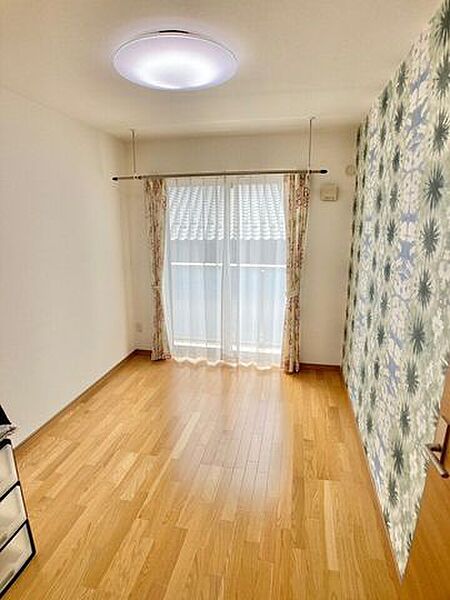 【ボタニカル柄の華やかなアクセントクロスが印象的な洋室】室内干し用ハンガーパイプが設置されており、雨の日や夜間の洗濯物干しもスムーズ。大きな窓から陽光が差し込む心地よい空間です。