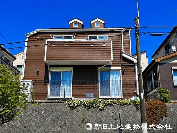 落ち着きのあるブラウンの外壁と白いアクセントが調和した、温もりを感じる外観デザイン。ワイドなバルコニーと個性的な屋根形状が住まいに表情を添え、緑豊かな植栽とともに、年月を重ねても飽きのこない上質です。