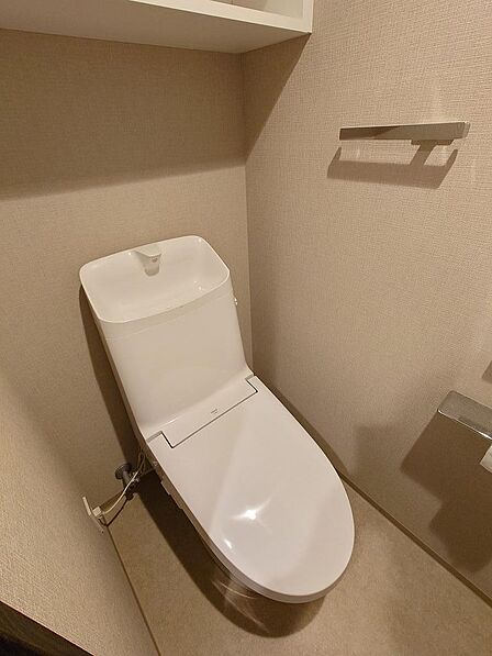 温水洗浄便座を備えた清潔感のあるトイレです。上部には棚が設けられ、ストック用品もすっきり収納できます。落ち着いた色合いの空間で、お子様から大人まで気持ちよくお使いいただけそうです。