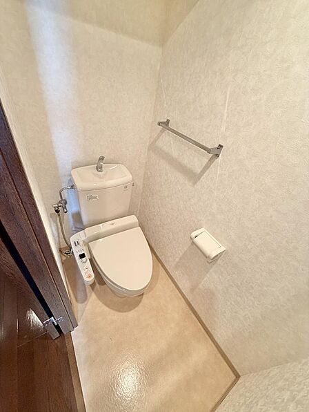 温水洗浄便座付きのトイレです。タオル掛けと紙巻器を備え、必要なものがコンパクトにまとまっています。落ち着いた色合いの壁紙で、清潔感のある空間です