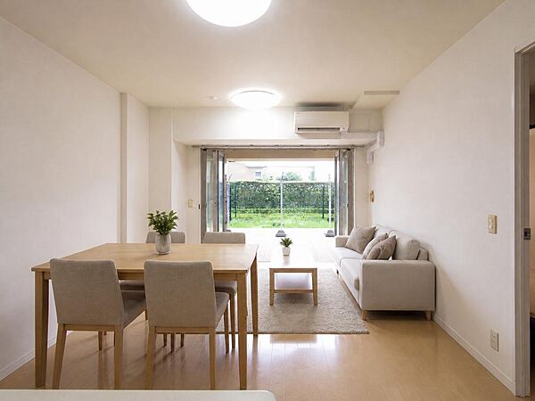約12帖のLDは対面キッチンで、調理中もご家族との会話を楽しめます。掃き出し窓の先には専用庭が広がり、陽光がたっぷり差し込む1階の角住戸です。※家具はバーチャルステージングによるイメージです