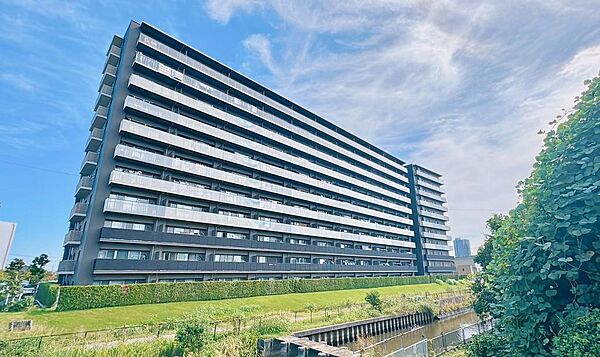 青空に映えるダークトーンの外観です。2018年1月築、鉄筋コンクリート造11階建の落ち着いたたたずまいで、建物沿いには生垣と芝生が広がります。ご家族で気持ちよく帰宅していただける環境です。