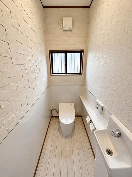 小窓から自然光を取り込めるトイレです。手洗いカウンターと温水洗浄便座が備わり、毎日気持ちよく使える清潔感のある空間です。明るさにもご注目ください。※AIによる家具消し加工を行なっております。