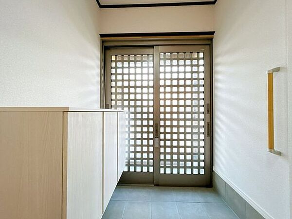 【リフォーム済】玄関ホールの写真です。壁天井はホワイト系クロスに張り替え、床もタイルをクリーニングしました。また、照明や大型のシューズボックスも新設してお客様を気持ちよく迎えられる玄関に仕上げました。