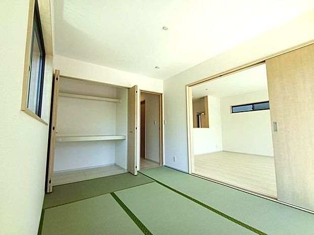 窓から光がたっぷり入る明るい和室で、畳の柔らかさと木目の温もりが調和し、収納も備えた使い勝手の良い落ち着いた空間です。