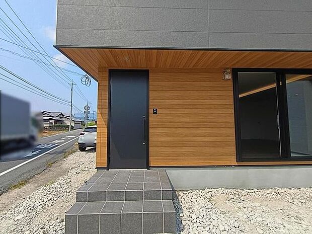 玄関まわりは木目とグレーが調和し、落ち着いた雰囲気をそっと演出します。ゆるやかに広がるアプローチが住まいへ心地よく迎え入れ、日々の暮らしにやさしい印象を添える空間です。
