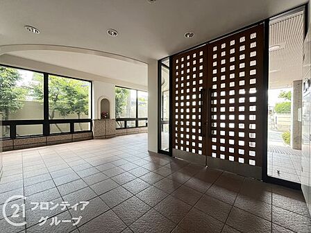 木製の格子スクリーンを設けたロビー。大判タイルの床と大きなガラス面で、共用部にゆとりと明るさがあります。玄関までは手すり付きのスロープと階段の2経路を確保しています。