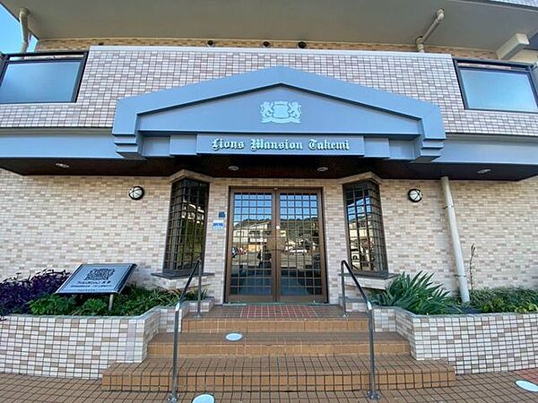 外壁にレンガ調のタイルが施されたエントランスです。扉の両脇には花壇が設けられ、多様な植栽が配置されています。