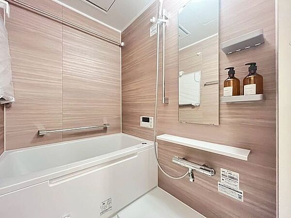 木目調の壁面パネルを採用した浴室です。浴槽横には手すりが設置され、安全性に配慮された設計となっています。また、小物類を置ける棚などの設備が備わっています。