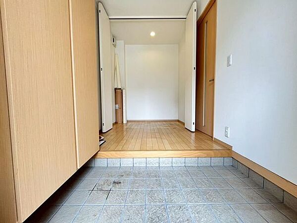 土間部分にはグレー系のタイルが敷かれています。左手には高さのある靴箱が配置され、正面には折れ戸で仕切られた空間が設けられています。