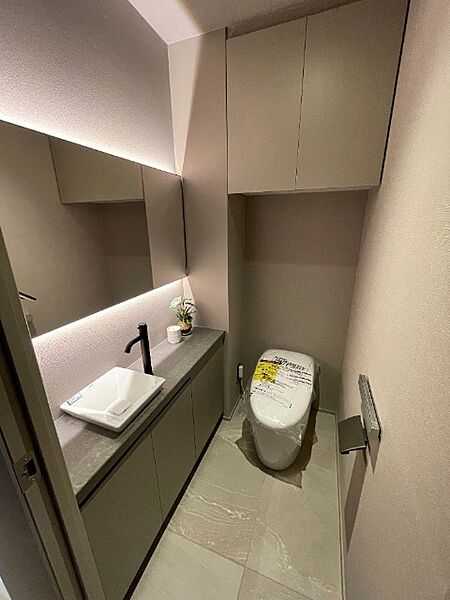 大きな鏡と独立手洗い器を備えたスタイリッシュなトイレ空間です！上部には扉付きの吊戸棚があり、トイレットペーパーや掃除用品を隠してスッキリ収納できますね♪ゲストも快適に利用できる上質な設備です！