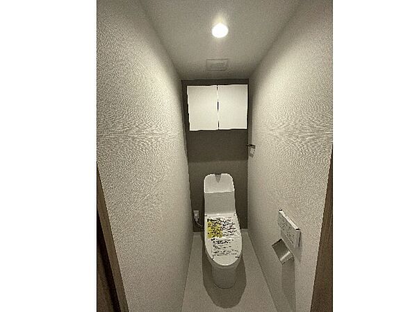 白を基調とした清潔感あふれるシンプルなトイレ空間です！上部にはトイレットペーパーのストックやお掃除用品を収納できる棚を備えており、床に物を置かずに足元を広く衛生的に保つことができる設計です