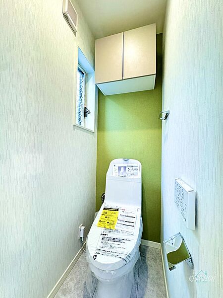 グリーンのアクセントクロスが爽やかな印象のトイレ。温水洗浄便座一体型便器と上部収納を備え、トイレットペーパーや小物も収納でき、すっきりとした使い勝手のよい空間です。