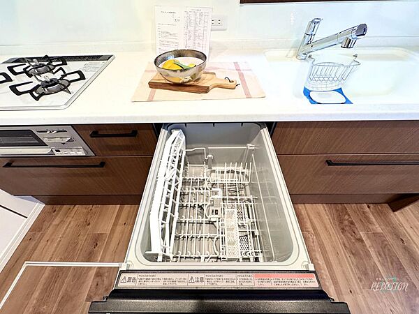 ビルトインタイプの食洗機がキッチン下部にすっきりと収まり、調理後の片付けを手軽にしてくれる実用的な空間。清潔感ある白いラックが印象的です。