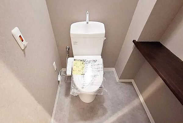清潔感のある温水洗浄便座付きトイレ。シックなアクセントクロスと利便性の高いカウンター棚を備え、落ち着いたプライベート空間に仕上がっています。