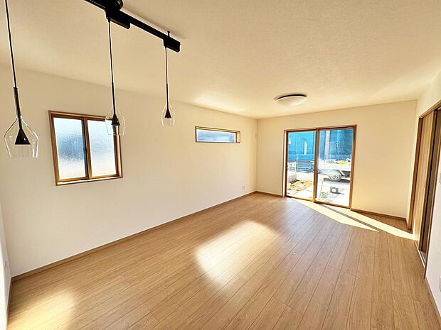 温かみのある木調の床が、穏やかな広がりを感じさせる空間。窓から入る光が、時とともに移ろう影を落とし、心地よいリズムを生み出します。シンプルなデザインの照明が、洗練された雰囲気を添えています。