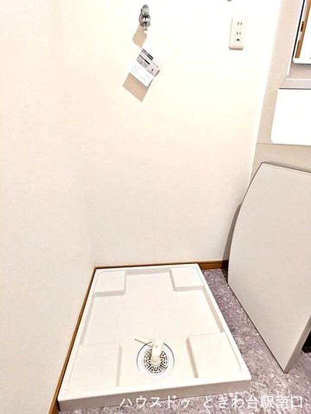 洗面室内の洗濯機置き場は、お手入れのしやすい防水パンを設置しています。周囲は清潔感のある白を基調としており、無駄のない配置で家事動線もしっかりと確保された、使い勝手の良い空間です。