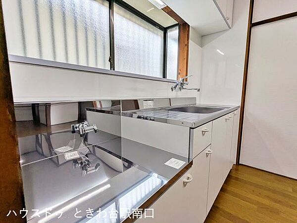 白い扉とステンレス天板が爽やかなキッチン。正面の窓から自然光を取り込めるため、明るい環境で調理できます。作業スペースと収納を備えた、使いやすい壁付けタイプです。