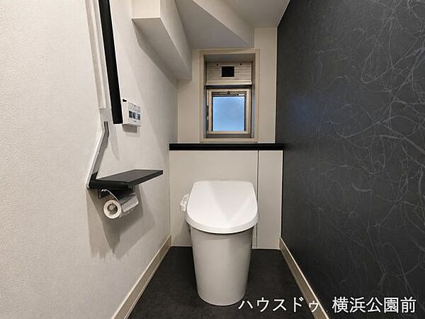 モダンで洗練されたトイレ空間。スタイリッシュなタンクレストイレを採用し、限られたスペースを広く美しく見せる工夫が施されています。手すりやカウンターも完備され、デザイン性と優しさを兼ね備えた設計です。