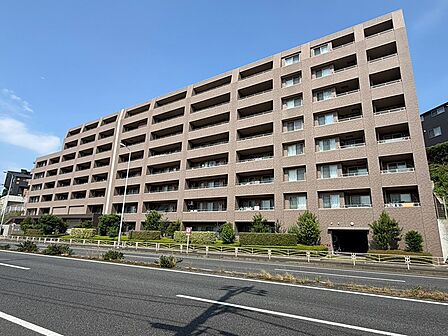 ブラウンの外壁が空に映える、堂々とした佇まいのマンション。植栽が配され、落ち着いた住環境です。開放感のある立地で、現地からの眺望も魅力。