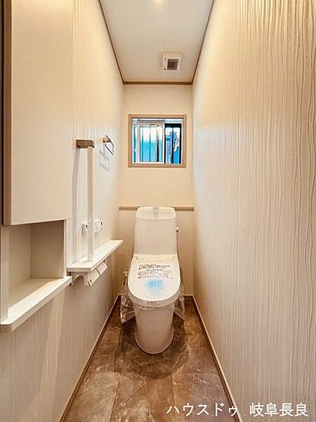 白を基調としたシンプルな壁紙のトイレです。手前のニッチには芳香剤を置いたり小物を置くことができますね