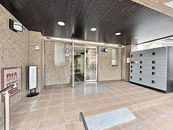落ち着いた色合いでまとめられたマンションエントランス。屋根付きで、雨の日も出入りしやすい快適な共用スペースです。