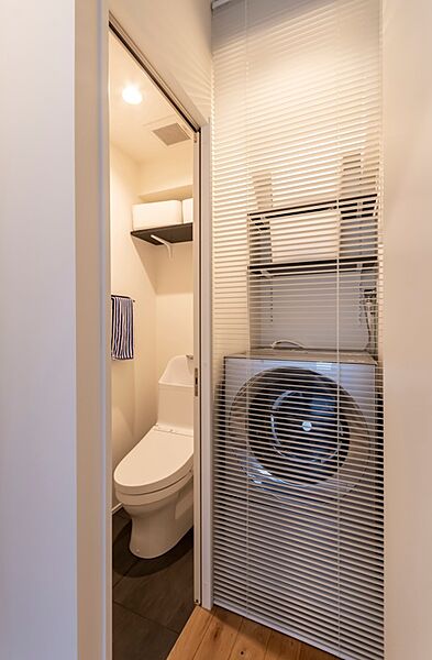 2022年12月リフォーム当初のトイレ。生活感を隠せるブラインド付きの洗濯機置き場と、上部収納でスッキリ使えるトイレ。限られたスペースを有効活用した、機能的でスタイリッシュな水回りです。