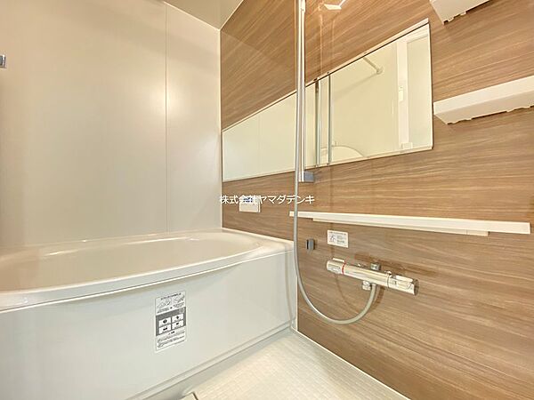 木目調の壁が落ち着いた雰囲気を醸し出す浴室です。ゆったりとした浴槽で、一日の疲れを癒すバスタイムをお過ごしいただけます。鏡やシャワーも備え付けられており、快適な暮らしをサポートします。