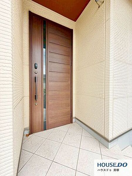 重厚感のある木目調の玄関ドアが印象的。屋根付きの玄関まわりで、雨の日の出入りも安心です。