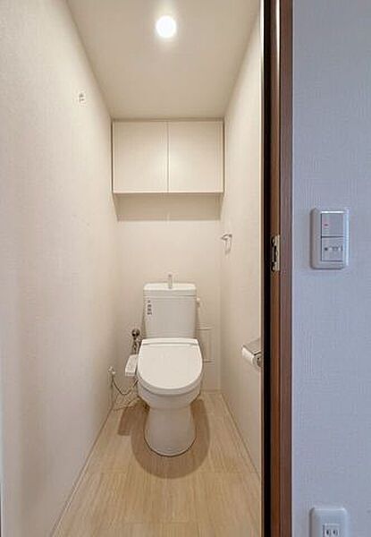 温水洗浄便座を備えた、清潔感あふれるレストルームです。上部にはトイレットペーパーや掃除用品をすっきりと収納できる吊り戸棚を備え、空間を美しく保てます。