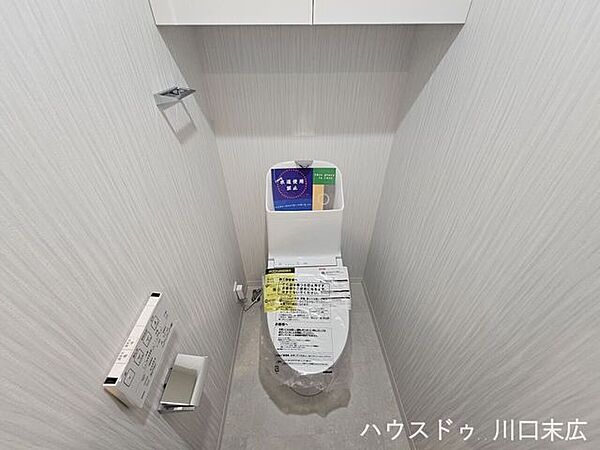 温水洗浄便座と上部吊戸棚を備えたトイレ空間。トイレットペーパーや清掃用品をスッキリと収納できます。