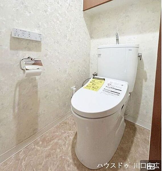 温水洗浄便座を備えた清潔感のあるトイレ空間です。上部には備品を収納できるキャビネットを設け、日常の利便性と整頓のしやすさに配慮した造りです。
