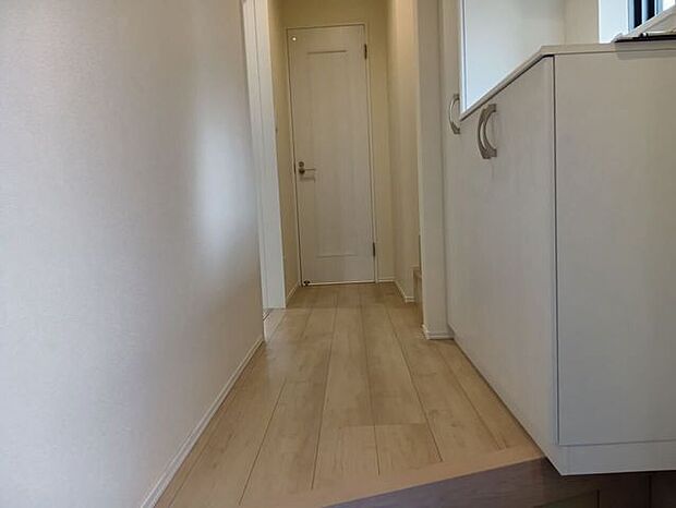 床材の木目が温もりを感じさせる玄関ホール。ホワイトを基調とした壁面と建具が空間を明るく見せ、清潔感のある第一印象を与えます。