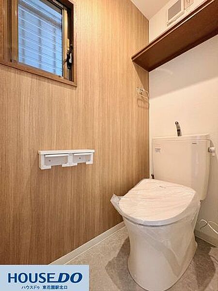 温かみのある木目調の壁紙が、落ち着いた雰囲気を演出するトイレ空間！小窓が付いているため、自然な光を取り入れながら換気もスムーズに行えます。上部にはトイレットペーパーなどを置ける棚付きです♪