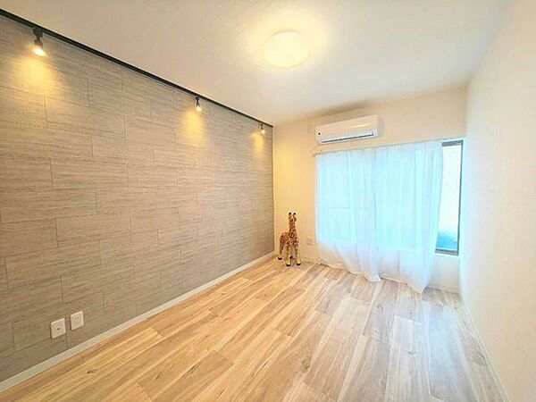 温かみのある木目調のフローリングと、柔らかな光が差し込む明るい室内。落ち着いた色調のアクセントウォールが、くつろぎの空間を演出します。