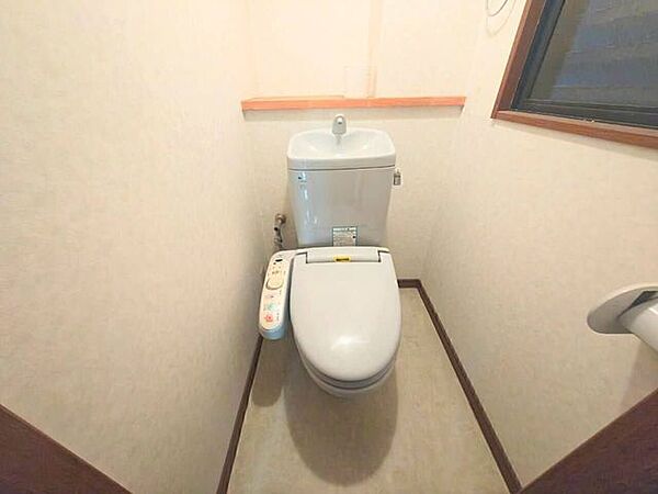 温水洗浄便座と手洗いタンクを備えた機能的なトイレです。小窓があり自然光が差し込むため、湿気やにおいがこもりにくく清潔さを保てます。木目の切り替えが落ち着いた空間を演出します。
