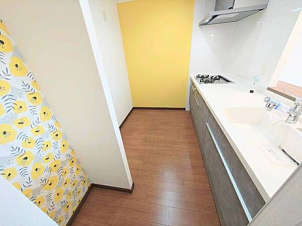 明るい黄色と花柄の壁紙が特徴のキッチン。朝の準備も楽しくなりそうな、元気になれる空間です。3口コンロと広々とした白い作業台、掃除がしやすい設計のレンジフードで清潔感が保たれます◎