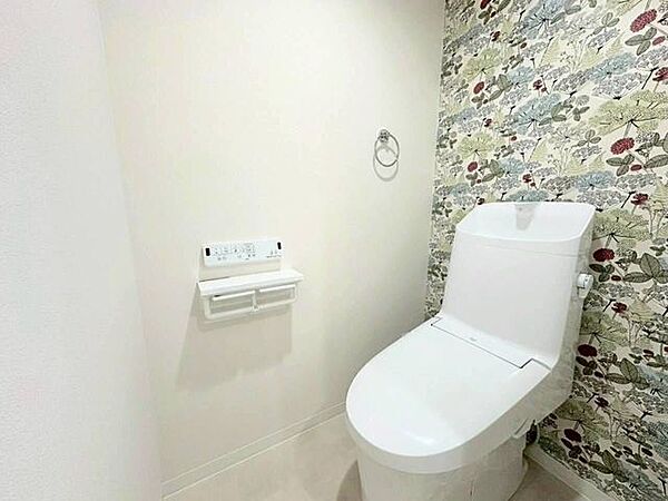 背面の壁にあしらわれたボタニカル柄のアクセントクロスが印象的なトイレ。白を基調としたシンプルな空間に、繊細な植物モチーフのデザインが程よい華やかさを添えています。