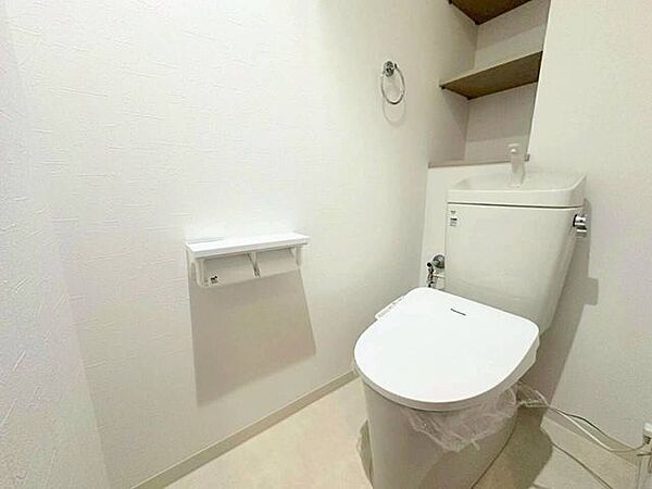 温水洗浄便座や手洗い付きタンク、2連ペーパーホルダーに加え、上部収納棚を備えたトイレ。ペーパーのストックや清掃用品をすっきり整理でき、快適に使用できる機能的な設備仕様です。