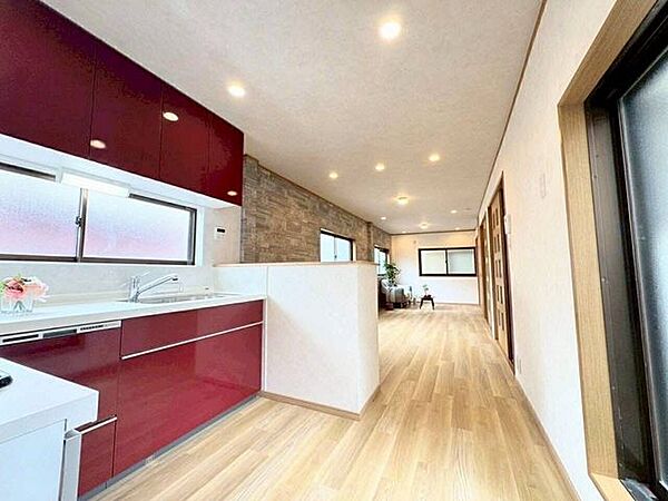 深みのあるワインレッドのシステムキッチンが空間のアクセント。奥に向かって縦長に広がるLDKは、木目調のフローリングと一部に施された石目調のアクセントクロスが調和する、洗練された内装デザインです。
