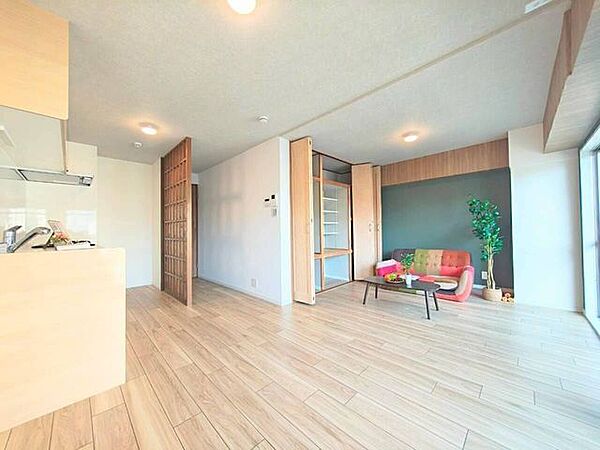大きな窓からやわらかな光が差し込む明るいLDK。木目の温もりを感じる内装と可動式の収納扉を備え、室内をすっきりと保ちながら心地よく過ごせる住空間です。